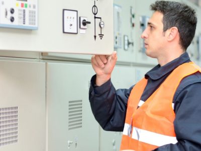 Electrician checks the condition of the equipment in control room. Man in protective workwear working in the power plant.